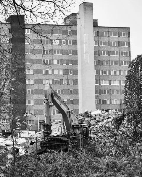Monochrome view of an excavator among rubble near a multi-storey building