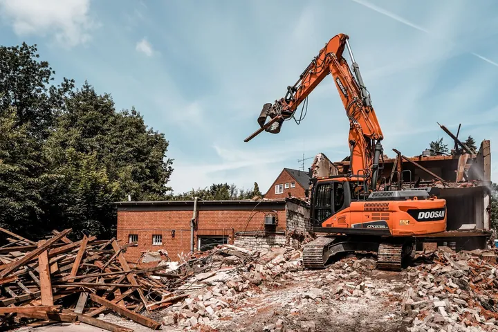 Orange excavator beside a partly demolished brick building