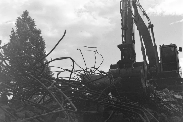 Monochrome view of an excavator and twisted steel at a demolition site