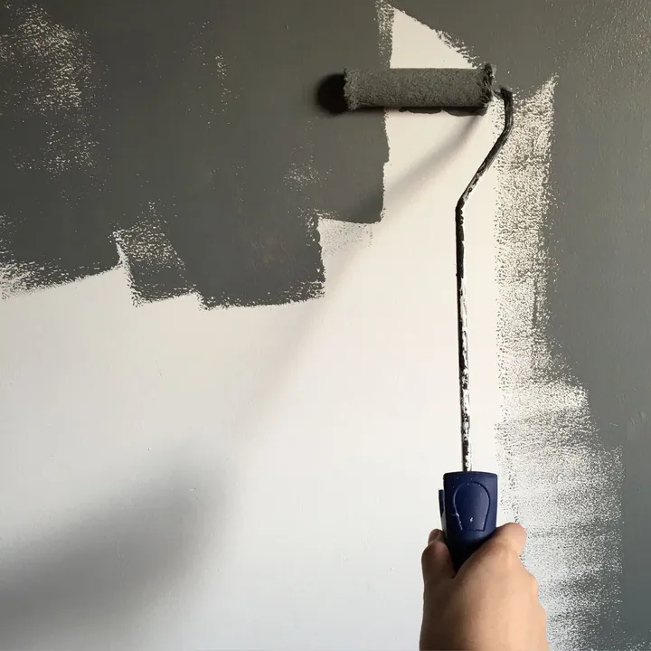 Paint roller applying dark paint to a pale wall