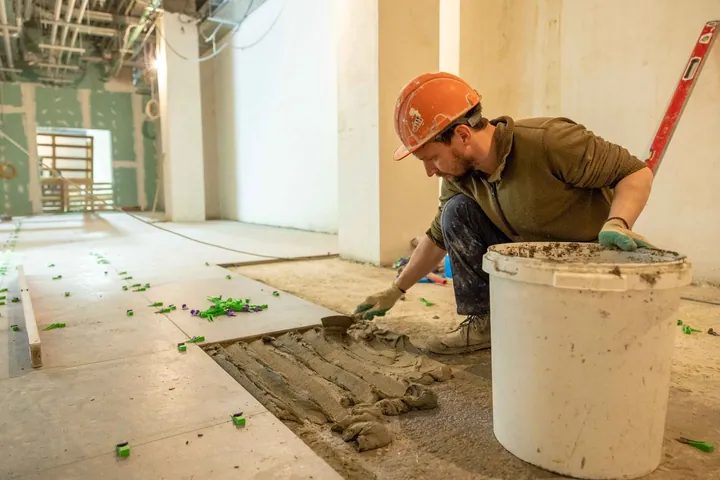 Worker laying floor tiles in an unfinished interior
